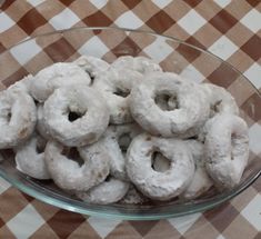 a glass bowl filled with powdered donuts on top of a checkered table cloth