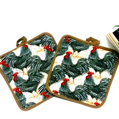 two square coasters with rooster and pine trees on them, one has a book in front of it