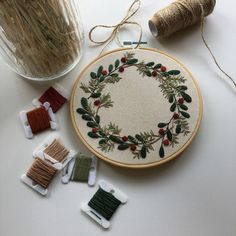 a cross stitch wreath surrounded by spools of thread and needles with other items on the table