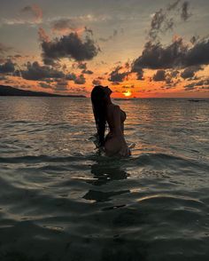 a woman is sitting in the water at sunset