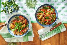 two bowls filled with stir fry vegetables on top of a wooden table next to green napkins