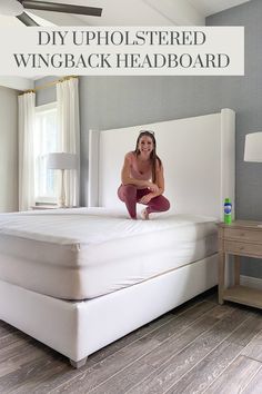 a woman sitting on top of a white bed in a room with wood flooring