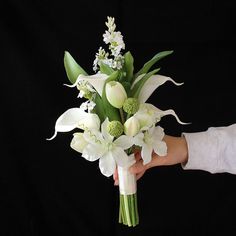 a bouquet of white flowers being held by a person's hand on a black background