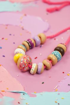 a colorful necklace with donuts and sprinkles on pink surface next to confetti