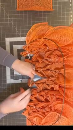 someone cutting fabric with scissors on top of a piece of orange material that is being sewn together