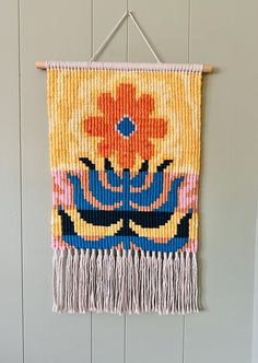 a woven wall hanging with an orange flower on it