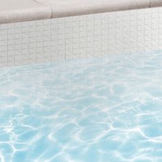 an empty swimming pool with blue water and white tiles on the wall, as well as a bench