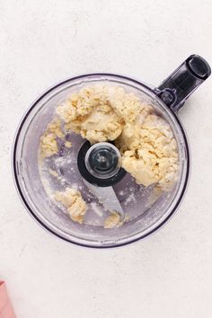 a food processor filled with dough on top of a white counter next to a pink napkin