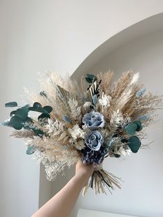 a hand holding a bouquet of flowers in it's left hand, against a white wall