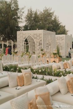 an outdoor wedding setup with white couches and pillows on the ground, surrounded by greenery