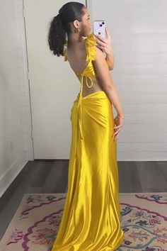 a woman in a yellow dress taking a selfie with her cell phone while standing on a rug