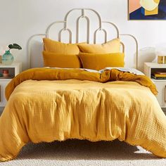 a bed with yellow linens and pillows in a white room next to a painting on the wall