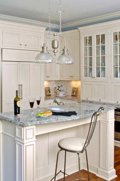 a white kitchen with an island and two wine glasses on the counter top next to it