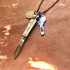 "-This rugged unisex necklace features a vintage pocket knife, a vintage key, and an old Columbian coin. -The trio hangs from a 29\" antique-silver chain with matching lobster clasp. -This unique necklace looks great on men or women. -The vintage pocket knife will be similar in size and color to the photos but each one is different. -Coin and key will also be similar but unique. -Designed and handmade in South Pasadena, CA. Check out more of our necklaces here: https://www.etsy.com/shop/ASTALIJe Vintage Jewelry With Lobster Clasp For Everyday, Vintage Brass Jewelry For Everyday Use, Vintage Brass Jewelry For Daily Use, Vintage Handmade Jewelry For Personal Use, Handmade Vintage Jewelry For Personal Use, Vintage Adjustable Necklaces For Everyday Use, Everyday Vintage Necklaces With Vintage Charm, Vintage Everyday Necklace, Pocket Knife Necklace