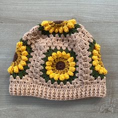 a crocheted hat with sunflowers on the front and bottom, sitting on a wooden surface