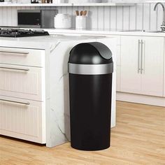 a black trash can sitting on top of a wooden floor next to a kitchen counter