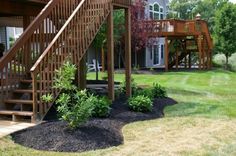 a wooden staircase leading up to a deck in a yard with grass and trees around it