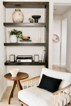 a white chair sitting in front of a wooden shelf filled with books and vases