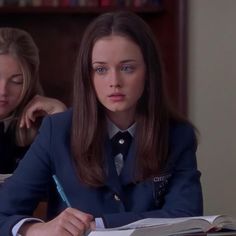 two women sitting at a table with pens and paper in their hands, one is writing