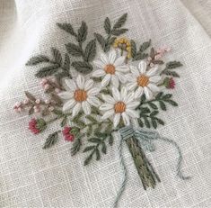 a bouquet of daisies and other flowers is stitched onto a white linen material