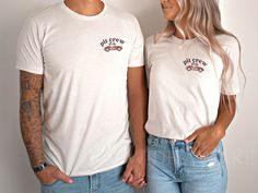 a man and woman standing next to each other in front of a white wall with tattoos on their arms