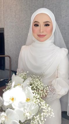 a woman in a white hijab holding a bouquet of flowers