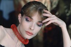 a woman with red and blue makeup is holding her hand to her head while wearing a necklace