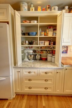 an organized kitchen with white cabinets and wood flooring is pictured in this image, there are many items on the shelves