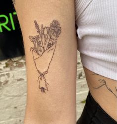 a woman with a tattoo on her arm has a bouquet of flowers wrapped in a ribbon