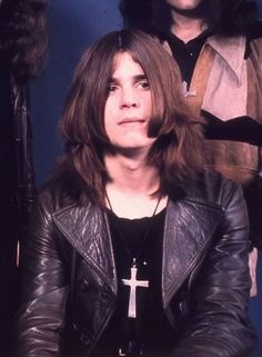 a man with long hair wearing a black leather jacket and standing next to another man