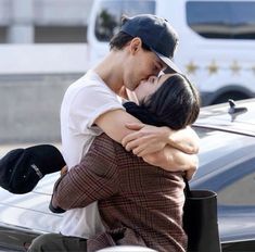 a man and woman hugging in front of a car