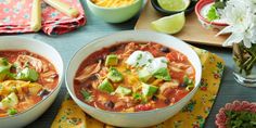 two bowls of mexican chicken soup with sour cream and avocado on the side