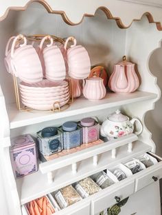 a white china cabinet filled with lots of pink dishes and cups on top of it