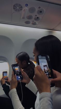 some people are taking pictures on their cell phones in an airplane while another person is looking at them