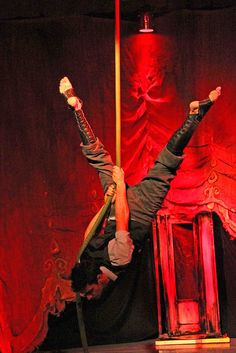 a man is upside down on a pole in front of a red curtain and stage