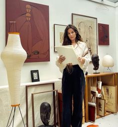 a woman is standing in an art studio holding a piece of paper and looking at the camera