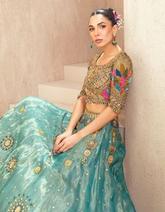 a woman in a blue and gold lehenga sitting on the steps with her hand on her hip