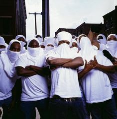 a group of men in white t - shirts and headscarves are standing together