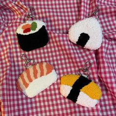 three sushi keychains on a red and white checkered table cloth,