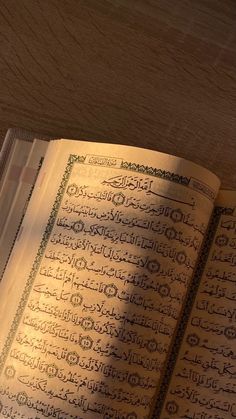 an open book with arabic writing on the page and light coming from behind it in front of a wooden table