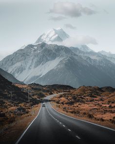 an empty road in the mountains with snow capped mountain peaks behind it and grass on both sides