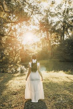 a girl in a white dress is walking through the grass with her back to the camera