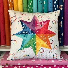 a multicolored star pillow sitting on top of a colorful bench in front of rainbow colored fabrics