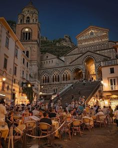 many people are sitting at tables in front of some buildings and stairs with lights on them