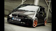 a small black car with orange rims parked in front of a building