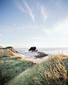 a small house on top of a hill by the ocean with grass growing around it