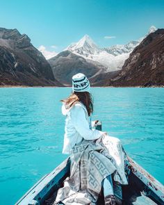 a woman sitting in the bow of a boat looking out at mountains and blue water