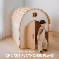 a young boy standing in front of a doll house made out of plywood planks