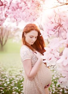 a pregnant woman is standing in front of pink flowers with her hands on her stomach