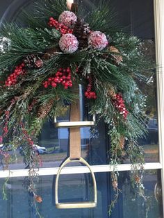 a christmas wreath hanging on the front door with pine cones, berries and evergreens